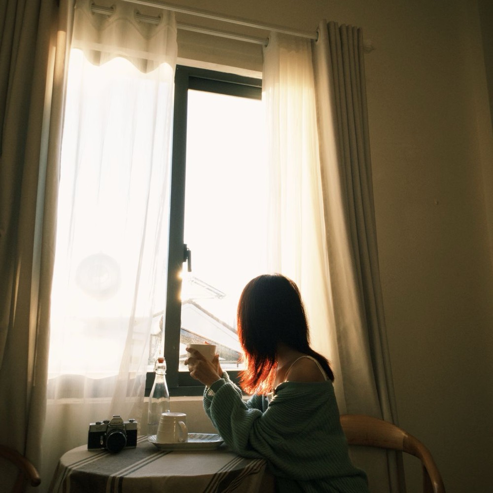 A woman with a coffee at a sunlit window in the morning