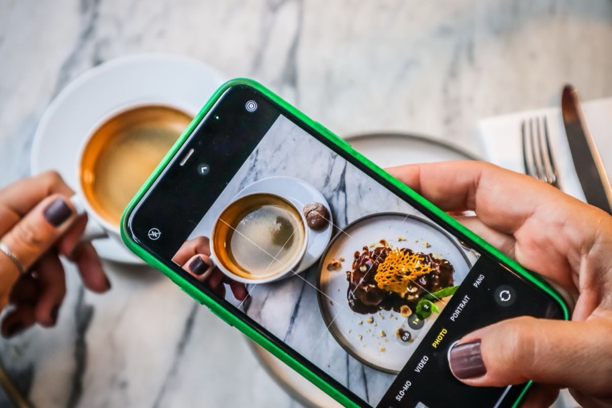 Someone photographing a plated dessert and a coffee with their phone
